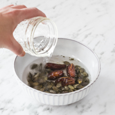 Jemand weicht die Bio-Datteln und Kürbiskerne in Wasser ein.