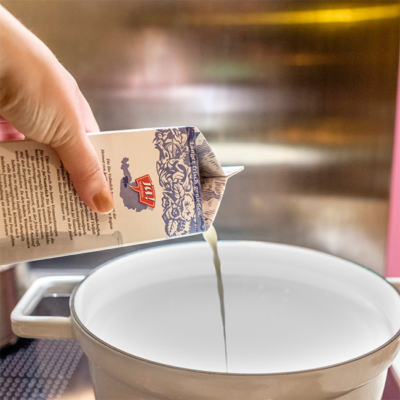 Jemand schüttet Ja! Natürlich Bio-Vollmilch in einen Topf.