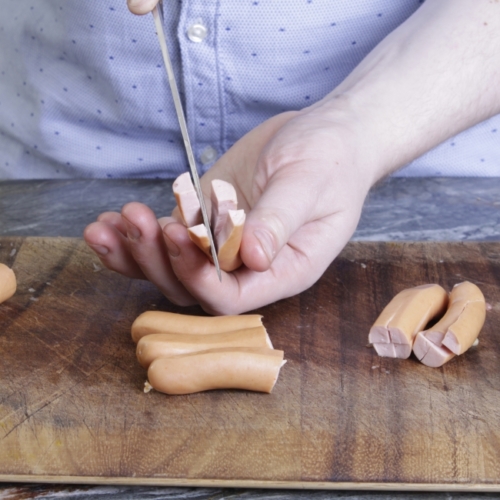 Jemand halbiert Bio-Würstel mit einem Messer.