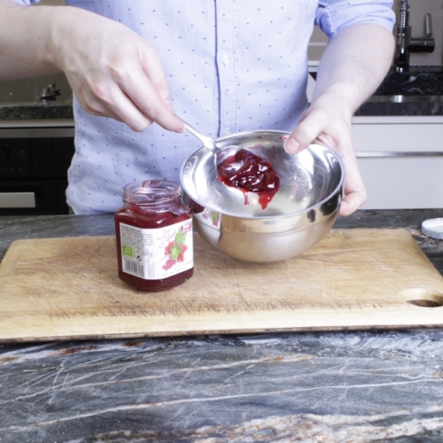 Jemand gibt Ja! Natürlich Preiselbeermarmelade in eine Schüssel.