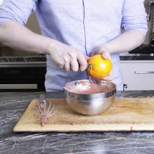 Jemand reibt die Schale einer Bio-Orange in eine Schüssel.