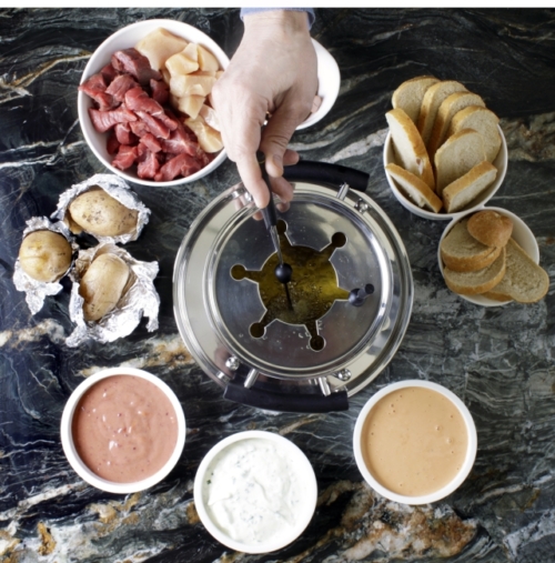 Fondue-Set mit einer Hand, die eine Fondue-Gabel in den Topf hält.