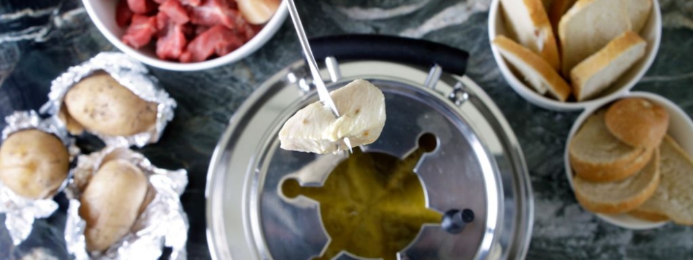 Nahaufnahme einer Hand, die ein Stück Hendlfleisch mit einer Fondue-Gabel hält.