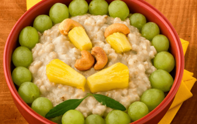 Jemand hält eine Schüssel mit Bio-Porridge mit Ananas, Weintrauben und Nussmix.