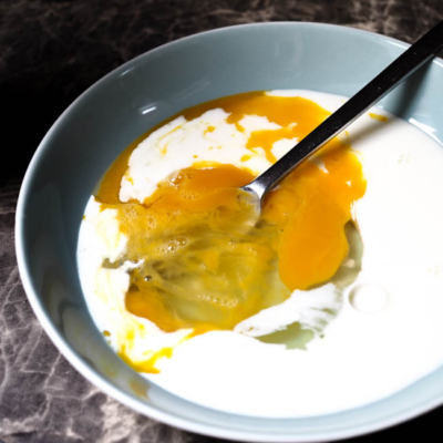 Milch, aufgeschlagene Eier und ein Löffel in einer Schüssel.