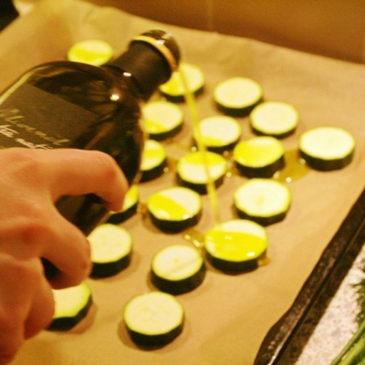 Jemand schüttet Bio-Olivenöl über Zucchinischeiben.