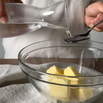 Jemand gießt Wasser über Bio-Butter in einer Schüssel.