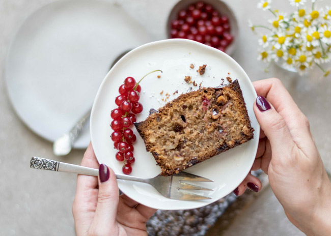 Bio-Zucchini-Schoko-Nuss-Kuchen auf einem Teller mit Gabel und Ribiseln.
