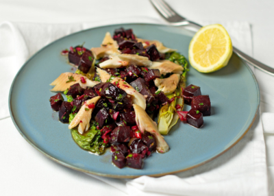 Roter-Bio-Rübensalat mit Saibling auf einem Teller mit einer Zitrone.