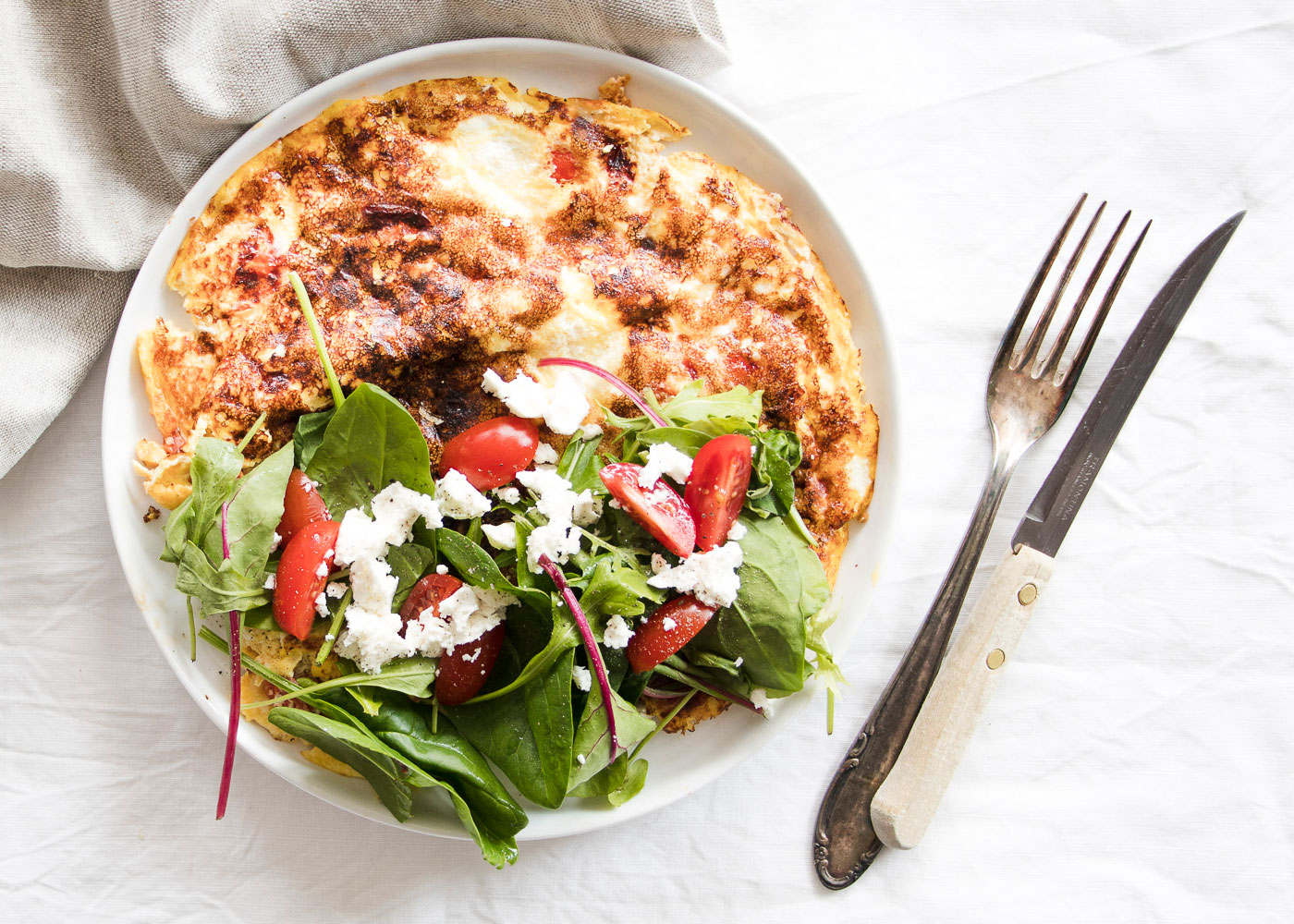 Mediterranes Omelette mit gemischtem Salat, Paradeisern und Bio-Feta auf einem Teller.