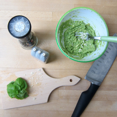 Marchfelder Bio-Erbsen Guacamole in einer Schüssel. Daneben ein Pfefferstreuer und Basilikum.