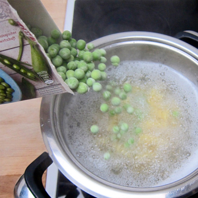 Jemand leert Bio-Erbsen in einen Topf mit kochendem Wasser.