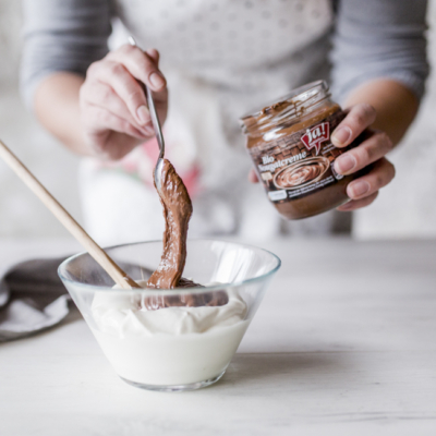 Jemand gibt einen Löffel Ja! Natürlich Bio-Nougatcreme in eine Schüssel.
