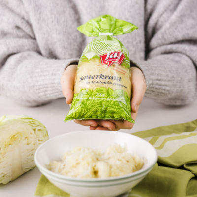 Jemand hält eine Packung Ja! Natürlich Bio-Sauerkraut, davor steht eine Schüssel mit dem Sauerkraut.