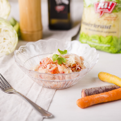 Eine Schüssel mit Karotten-Krautsalat, im Hintergrund eine Packung Ja! Natürlich Bio-Sauerkraut.