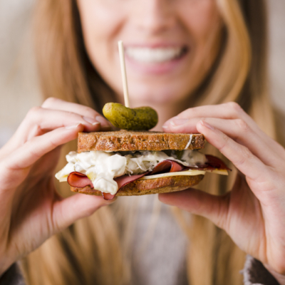 Eine Frau hält ein Sandwich, gefüllt mit Ja! Natürlich Sauerkraut, einem Schinkenblatt und einem Gurkerl.