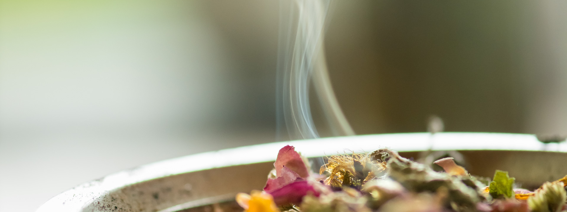 Nahaufnahme einer feuerfesten Schale mit verschiedenen Kräutern. Eine kleine Rauchschwade steigt über den Kräutern auf.