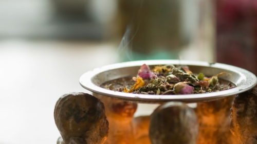 Eine feuerfeste Schale mit verschiedenen Kräutern. Eine kleine Rauchschwade steigt über den Kräutern auf.