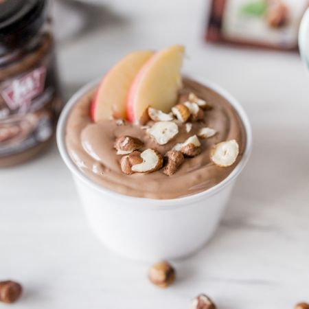 Nougat-Dessert in einer Schüssel mit zwei Apfelscheiben und Bio-Haselnüssen.