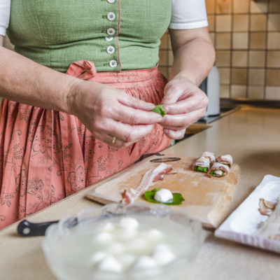 Jemand umwickelt die Spinatblätter mit Mozzarella und Bio-Speck.