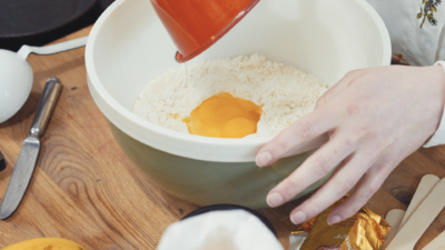 Jemand leert aufgeschlagene Bio-Eier in eine Schüssel mit Mehl.