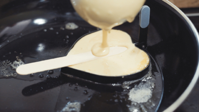 Pfannkuchenteig wird in eine Herzform in einer Pfanne gegossen.