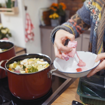 Jemand gibt Bio-Rindermarkknochen in einen Suppentopf mit geschnittenem Gemüse und Rindfleisch.