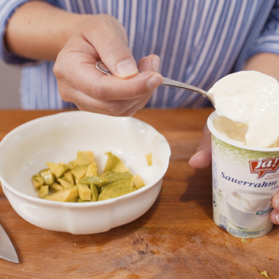 Jemand gibt Ja! Natürlich Bio-Sauerrahm in eine Schüssel mit Avocadostücken.