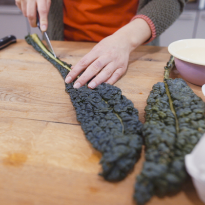 Jemand zerschneidet Bio-Schwarzkohlblätter auf einem Holzbrett.