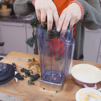 Jemand gibt zerkleinerte Bio-Schwarzkohlblätter in einen Standmixer.