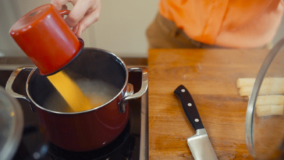 Jemand kippt eine Tasse voll gefüllt mit Bio-Polenta ins kochende Wasser.