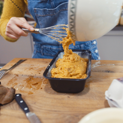 Jemand schüttet den Teig von Bio-Süßkartoffel-Bananenbrot in eine Backform.