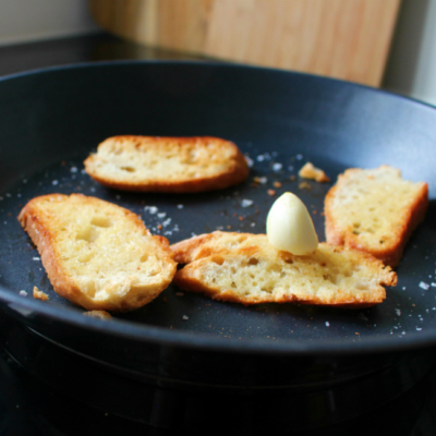 Brotscheiben in einer Pfanne mit einer Bio-Knoblauchzehe.