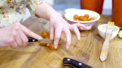Jemand schneidet Bio-Paradeiser auf einem Schneidebrett.
