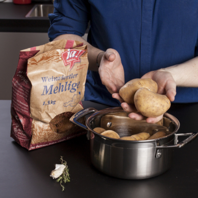 Jemand hält mehlige Ja! Natürlich Bio-Kartoffeln über einem Topf in den Händen.