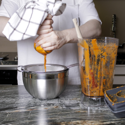 Jemand siebt Karottenpüree durch ein Tuch.