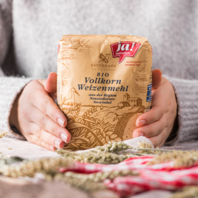 Jemand hält eine Packung Ja! Natürlich Bio-Vollkorn-Weizenmehl in den Händen.