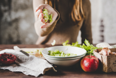 Jemand lässt Bio-Salat in eine Schale fallen.