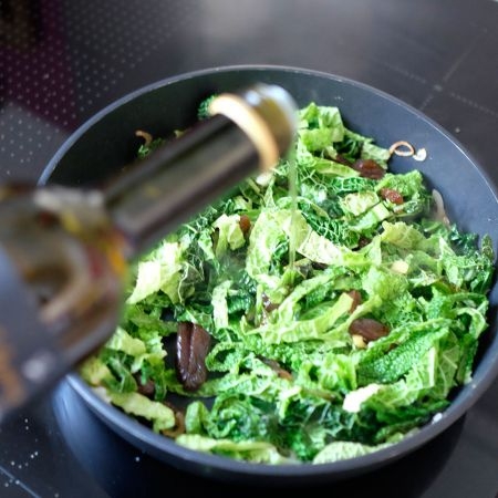 Jemand schüttet Olivenöl über einen Bio-Kohlsalat.