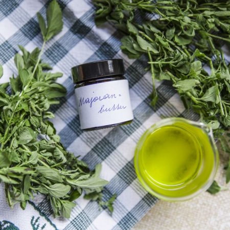 Ein Geschirrtuch auf dem Bio-Majoran liegt und ein Messbecher mit Majoransalbe.