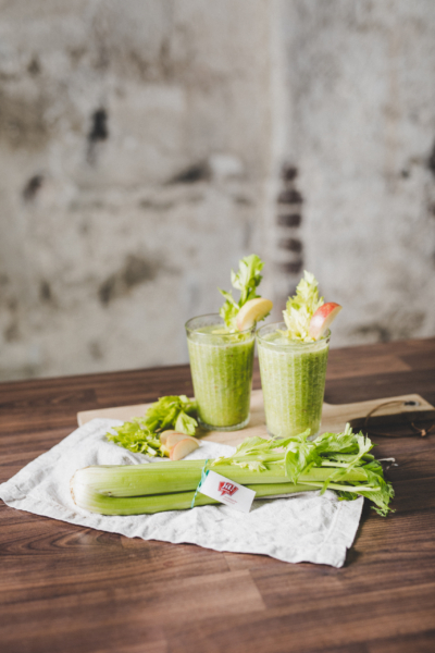 Zwei Gläser grüner Smoothies mit Bio-Stangensellerie davor.