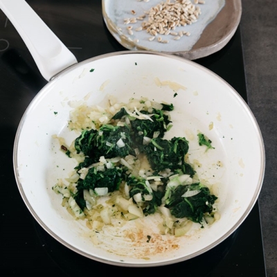 Bio-Schalotte, Knoblauch und Blattspinat in einer Pfanne.