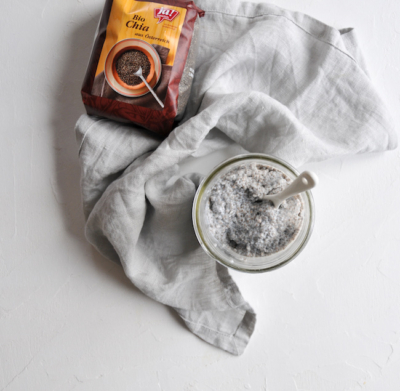 Chia-Samen in einem Gefäß vermengt mit Buttermilch, daneben eine Verpackung Ja! Natürlich Bio-Chia-Samen.