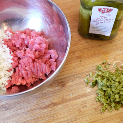 Eine Schüssel mit Bio-Faschiertem und Zwiebel, daneben Ja! Natürlich Bio-Delikatess Gurkerl.