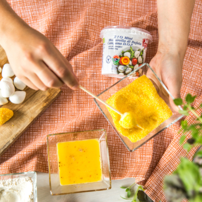 Jemand wälzt Ja! Natürlich Bio-Mozzarella-Minis in Polenta zum Panieren.