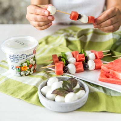 Jemand macht Spieße aus Wassermelone und Ja! Natürlich Bio-Mini-Mozzarella-Bällchen.