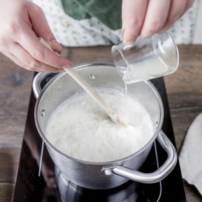 Jemand leert Zitronensaft in einen Topf mit kochender Bio-Heublumenmilch.
