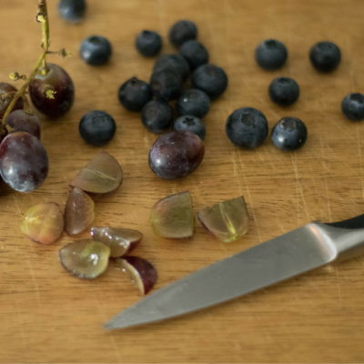 Geschnittene Bio-Weintrauben und Heidelbeeren auf einem Schneidebrett.