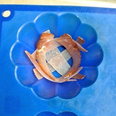 Jemand legt Bio-Speckstreifen kreuzweise in eine Muffinmulde.