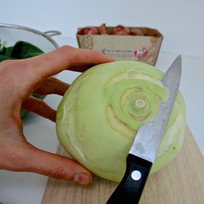 Jemand entfernt den Strung eines Bio-Kohlrabis. Im Hintergrund steht ein Karton mit Ja! Natürlich Bio-Schalotten.